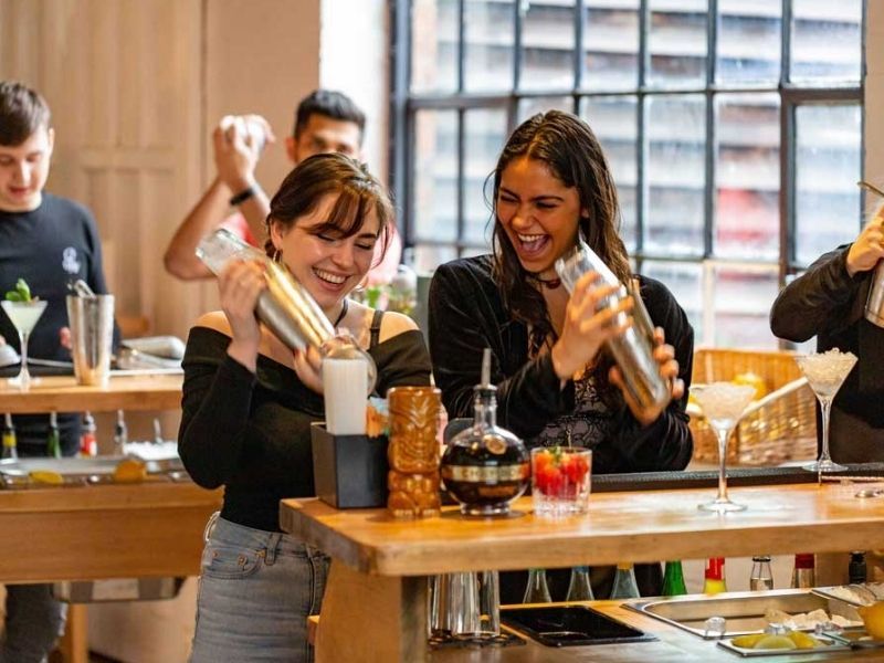 Compañeras agitando cocteleras en un taller de combinados antes de la cena